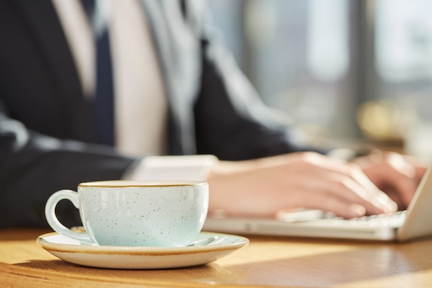 Foco seletivo em uma xícara de café, homem de negócios, trabalhando no laptop em fundo