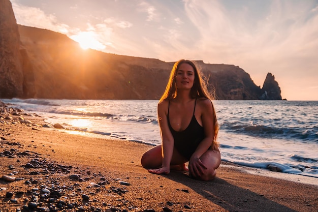 Foco seletivo feliz mulher sensual despreocupada com cabelos longos em trajes de banho pretos posando na praia do sol