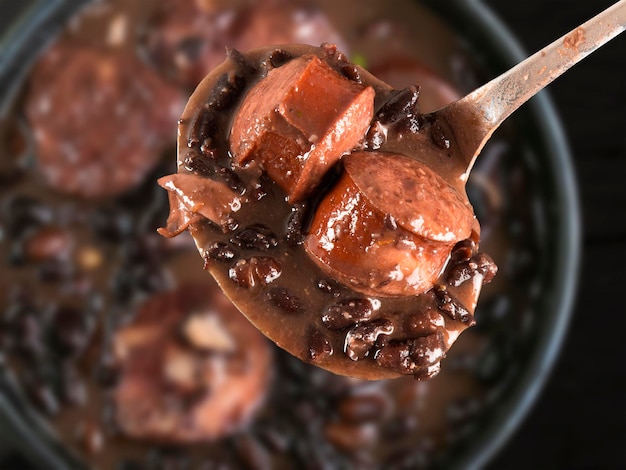 Foto foco seletivo na colher com comida brasileira de feijoada comida tradicional brasileira feita com feijão preto