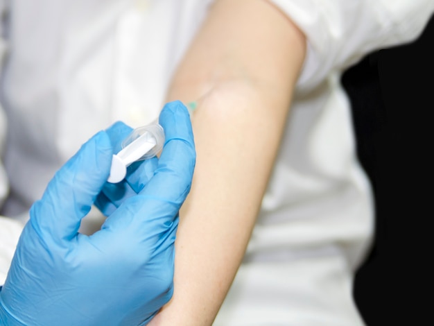 Foto foco seletivo na mão do médico na luva de látex azul com seringa, dando a injeção