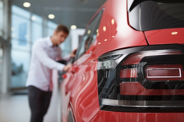 Foco seletivo nas luzes do carro, cliente do sexo masculino examinando o carro na concessionária em segundo plano