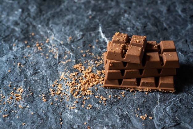 Foto foco seletivo pedaços de chocolate quebrado e cacau em pó no fundo de pedra