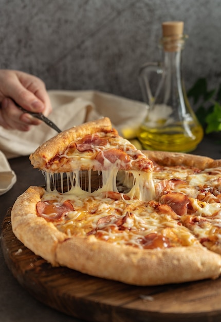 Foco seletivo pizza quente com queijo e calabresa a garota puxa uma fatia de pizza com queijo derretido alongamento posição vertical humor sombrio