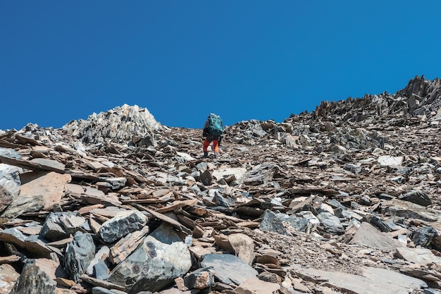 Foco seletivo. Subida pesada em uma encosta íngreme de pedra. Caminhada solo nas montanhas. Estilo de vida de fotógrafo de viagens, trilhas difíceis, conceito de aventura nas férias de primavera.