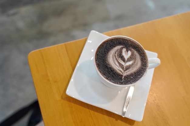 Foto foco seletivo vista de um café cappuccino na mesa de madeira no café com fundo de luz solar uma xícara de chocolate quente na mesa sobremesas e doces férias e romance