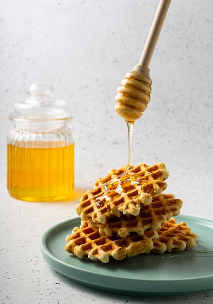 Foco seletivo, waffles de açúcar belgas com mel de flores em um prato azul