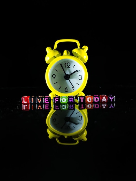 Foto foco seletivoum relógio amarelo e a palavra live for today em um dado preto com reflexo em um fundo preto
