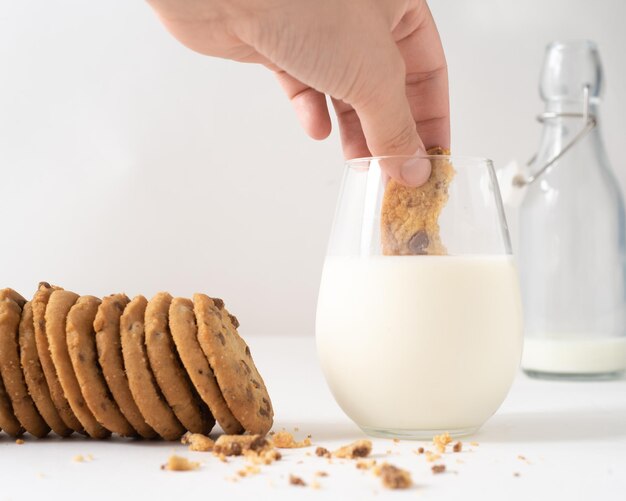 Foco suave de una persona sumergiendo una galleta con trocitos de chocolate en un vaso de leche