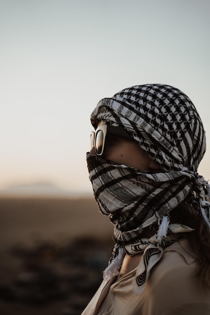 Foco superficial de una persona con gafas de sol y un pañuelo alrededor de la cabeza en un desierto por la noche