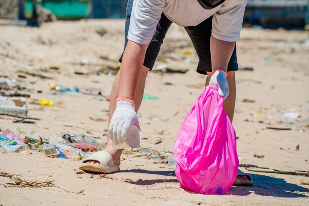 Focus Hombre voluntario con guantes recogiendo basura de botellas en la playa del parque Limpieza de la naturaleza