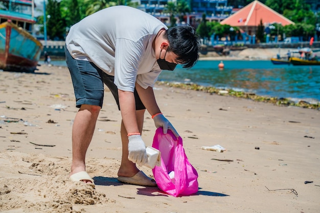 Focus Hombre voluntario con guantes recogiendo basura de botellas en la playa del parque Limpieza de la naturaleza
