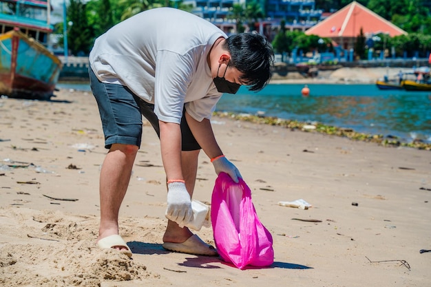 Focus Hombre voluntario con guantes recogiendo basura de botellas en la playa del parque Limpieza de la naturaleza