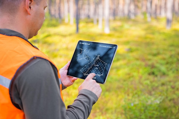 Förster mit Tablet-Computer im Wald und Blick auf die topologische Karte oder den Landplan auf dem Bildschirm