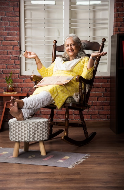 Foto fofa senhora indiana asiática sênior sentada em uma cadeira reclinável ou sofá lendo um livro ou usando a guia ou o computador laptop