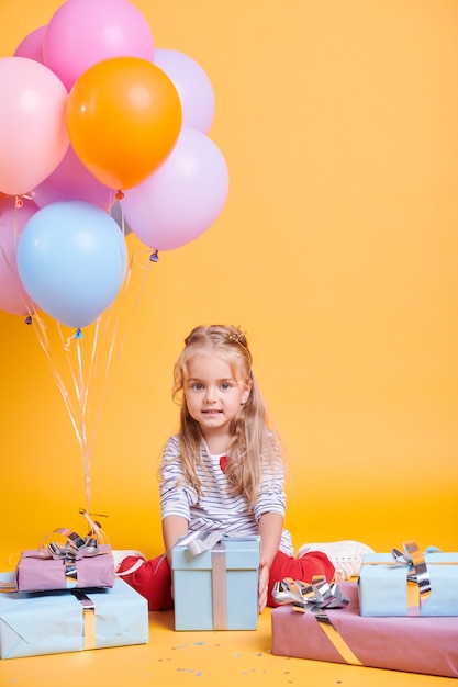 Fofinha casual com um presente posando na parede amarela isolada durante a festa de aniversário