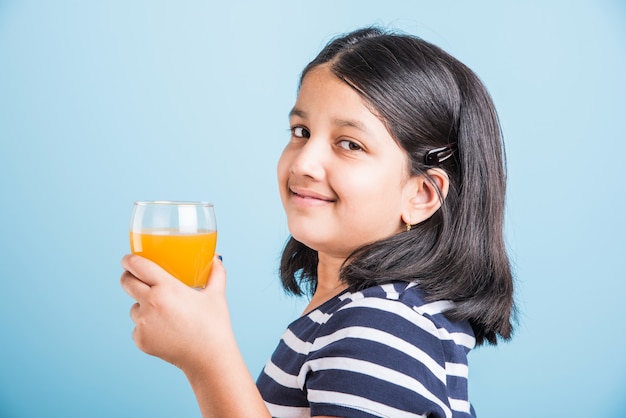 Fofinho menina indiana ou asiática brincalhona bebendo manga fresca ou suco de laranja ou bebida gelada ou bebida em um copo, isolado sobre fundo branco