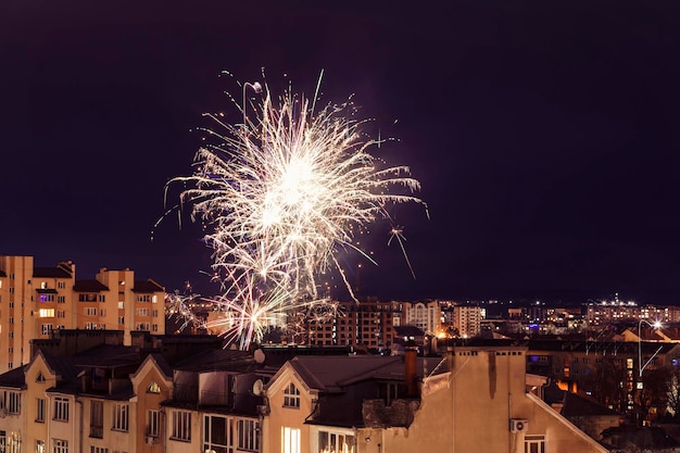 Fogo de artifício na cidade à noite com telhado de edifícios. Copie o espaço. Fundo festivo de fogos de artifício