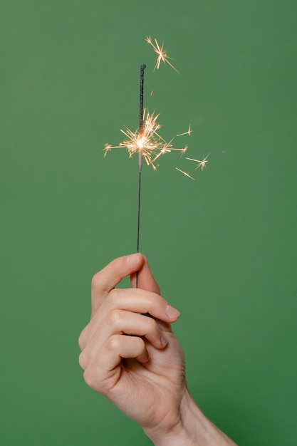 Fogo de Bengala queimando na imagem vertical de fundo verde isolada Mão feminina segurando estrelinhas Conceito de férias de inverno