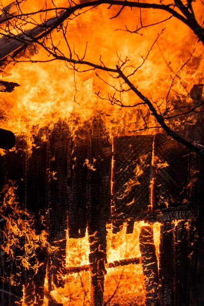 Fogo em todos os lugares e fumaça em uma área residencial à noite. Fogo perigoso. Casa inteira e quintal em chamas. Um incêndio destrói uma casa queimada carbonizada. carbonizado em casa de chamas à noite.