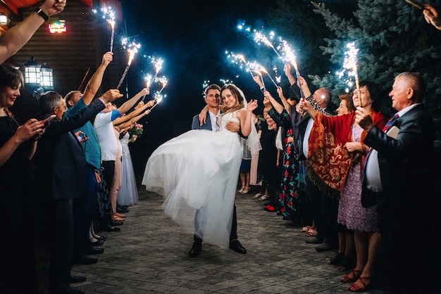 Fogo frio de velas de bolo e fogos de artifício nas mãos das pessoas ao redor dos recém-casados