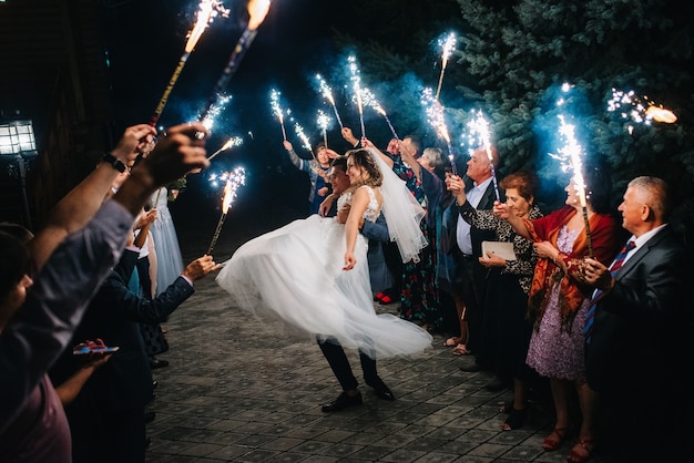 Fogo frio de velas de bolo e fogos de artifício nas mãos das pessoas ao redor dos recém-casados