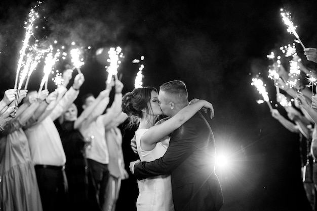 Fogo frio de velas de bolo e fogos de artifício nas mãos das pessoas ao redor dos recém-casados