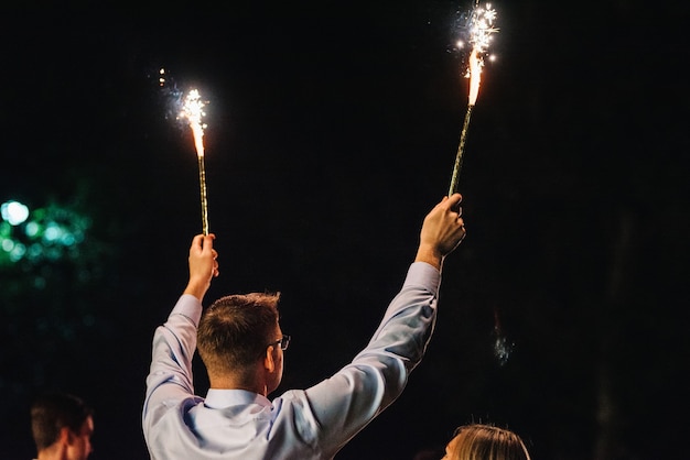 Fogo frio de velas de bolo e fogos de artifício nas mãos das pessoas ao redor dos recém-casados