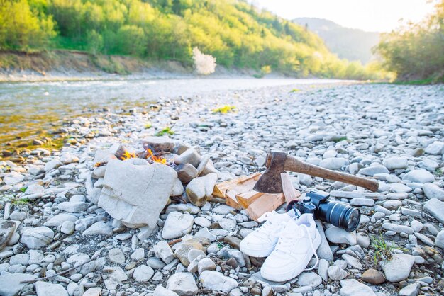 Fogueira de acampamento com lenha e machado perto dele no pôr do sol tênis branco com câmera dslr