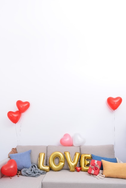 Foil Liebesballons und Geschenke auf einem Sofa mit weißer Wand im Hintergrund zum Valentinstag, Überraschungskonzept zum Muttertag.