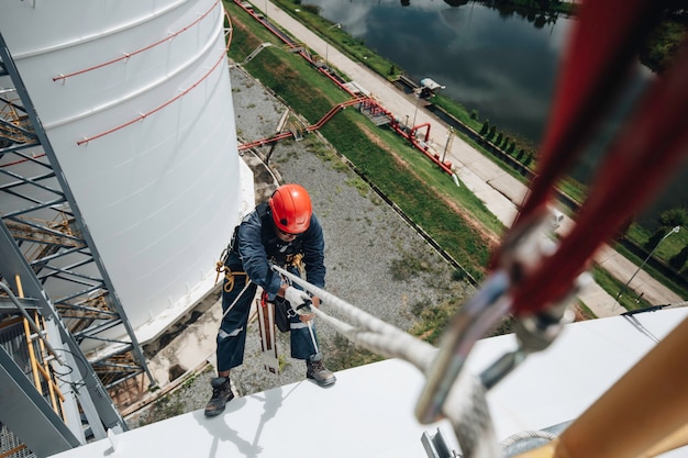 Fokus Draufsicht männlicher Arbeiter unten Karabinerseilhöhe Tankdachknoten Handlauf Seilzugangssicherheitsinspektion des Dickenspeicherdachs.