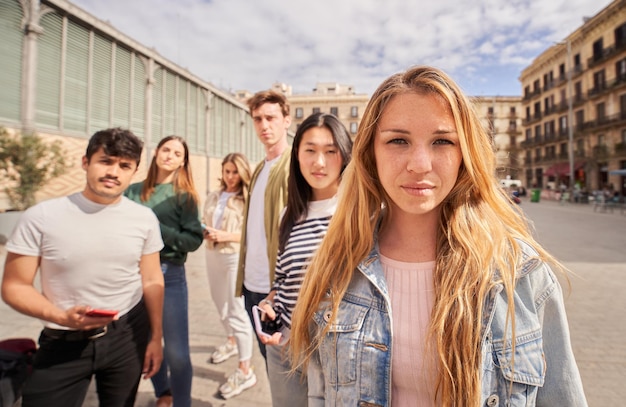 Fokus ernsthafte junge blonde Frau schaut in die Kamera auf der Straße Gruppe multiracial Freunde im Hintergrund