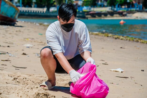 Fokus Freiwilliger Mann mit Handschuhen, der Flaschenmüll am Parkstrand sammelt Naturreinigung