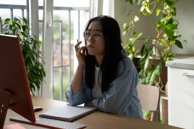 Fokussierte asiatische Studentin, die zu Hause studiert und an einem virtuellen Unterricht teilnimmt, der einen Online-Kurs belegt
