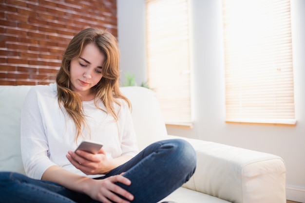 Fokussierte Frau, die auf der Couch unter Verwendung ihres Telefons im Wohnzimmer sitzt