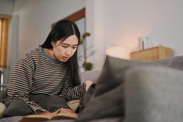Fokussierte freiberufliche Frau mit Laptop auf der Couch, die ein Online-Webinar sieht und eine Nachricht liest