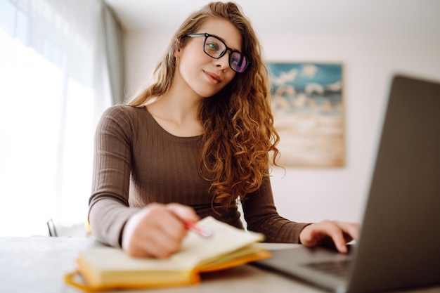 Fokussierte junge Frau sitzt an einem Tisch mit Laptop und hellem Notizblock Konzept des freiberuflichen Urlaubs