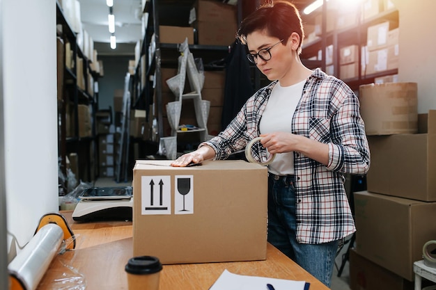 Fokussierte kurzhaarige Lagerarbeiterin, die einen Karton verpackt