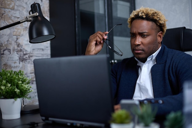 Fokussierter afrikanischer Geschäftsmann, der auf einen Laptop schaut, der Forschung betreibt