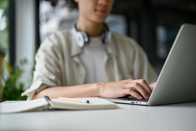 Fokussierter asiatischer männlicher Student, der auf der Tastatur tippt und mit einem Laptop im Internet surft