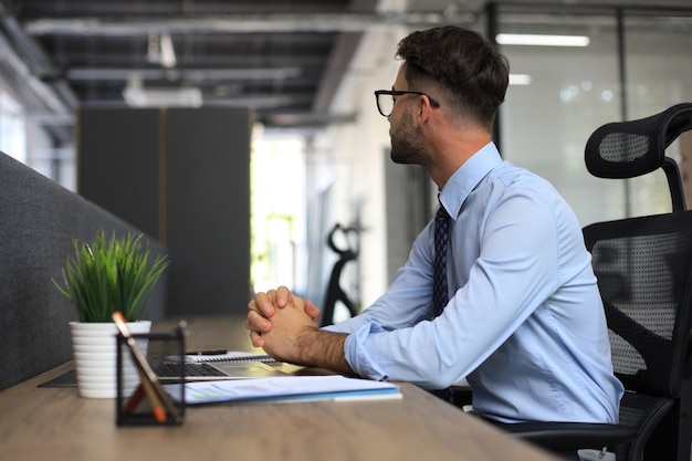 Fokussierter Geschäftsmann, der in einem modernen Büro in eine Berichtsdatei denkt, die Börsengewinne berechnet, Startup-Geschäft.