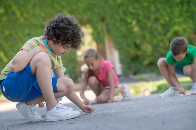 Fokussierter Junge mit Freunden, die auf Asphalt malen