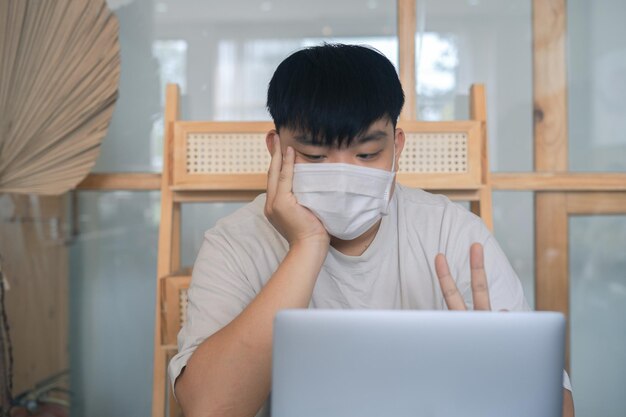 Fokussierter junger Mann mit medizinischer Maske, der mit einem Laptop auf der Tastatur E-Mails schreibt