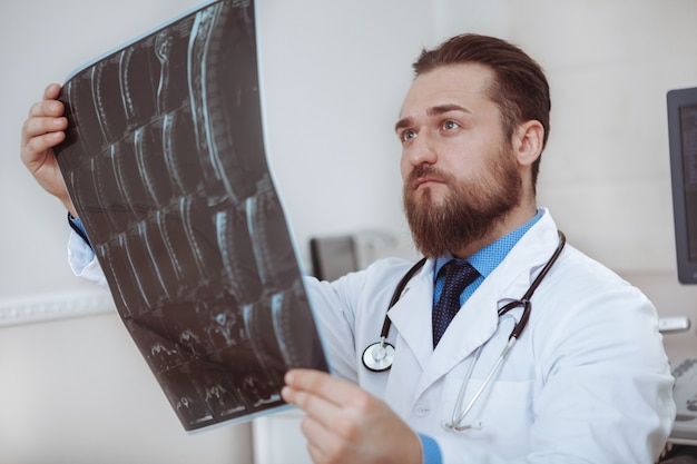 Fokussierter männlicher medizinischer Arbeiter, der MRT-Scans eines Patienten betrachtet