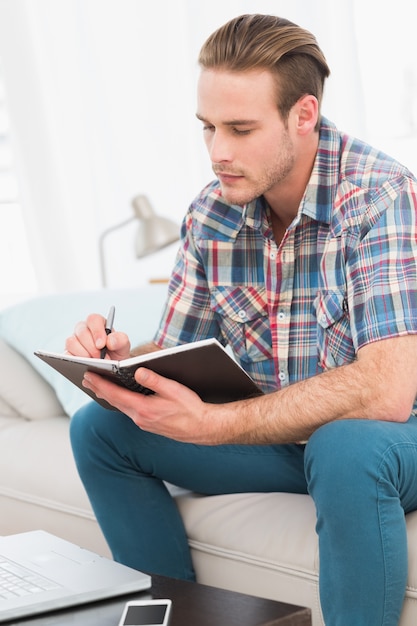 Fokussierter Mann auf einem Laptop mit einem Notizbuch