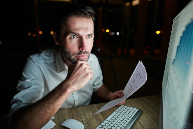 Fokussierter Mann, der nachts ein Dokument analysiert