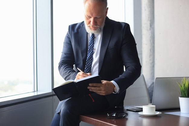 Fokussierter reifer Geschäftsmann, der in seinem modernen Büro arbeitet und Notizen macht.