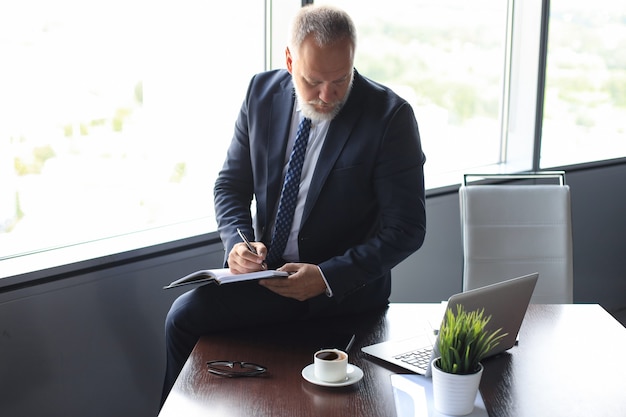 Fokussierter reifer Geschäftsmann, der in seinem modernen Büro arbeitet und Notizen macht.