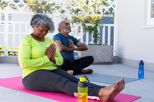 Fokussiertes afroamerikanisches Seniorenpaar praktiziert Yoga auf Matte im Garten. Aktiver und gesunder Ruhestandslebensstil zu Hause.