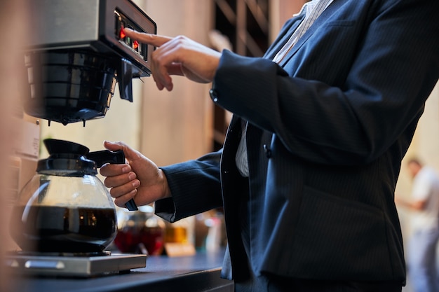 Fokussiertes Foto auf weiblicher Hand, das beim Aromakaffee die Taste drückt