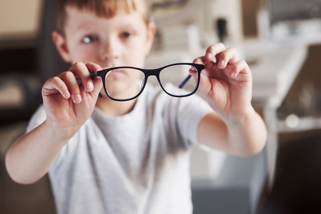 Fokussiertes Foto. Kleiner Junge hält seine neue Brille in der Arztpraxis.